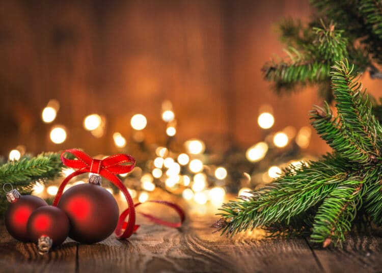 Red Christmas Ornaments on Wood Background and defocused lights. Spruce Tree branch on the left and right.