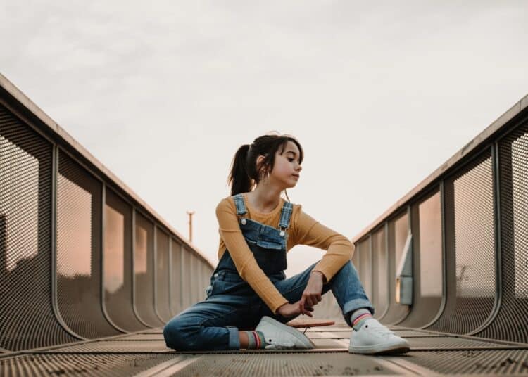 Girl sitting on skateboard on walkway