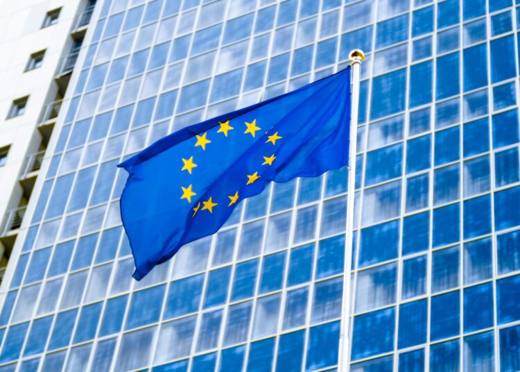 image of eu flag fluttering on wind against high business office building made of concerete and
