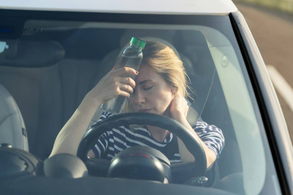 exhausted girl driver suffering from headache heat hot weather applies bottle of water to forehead 1
